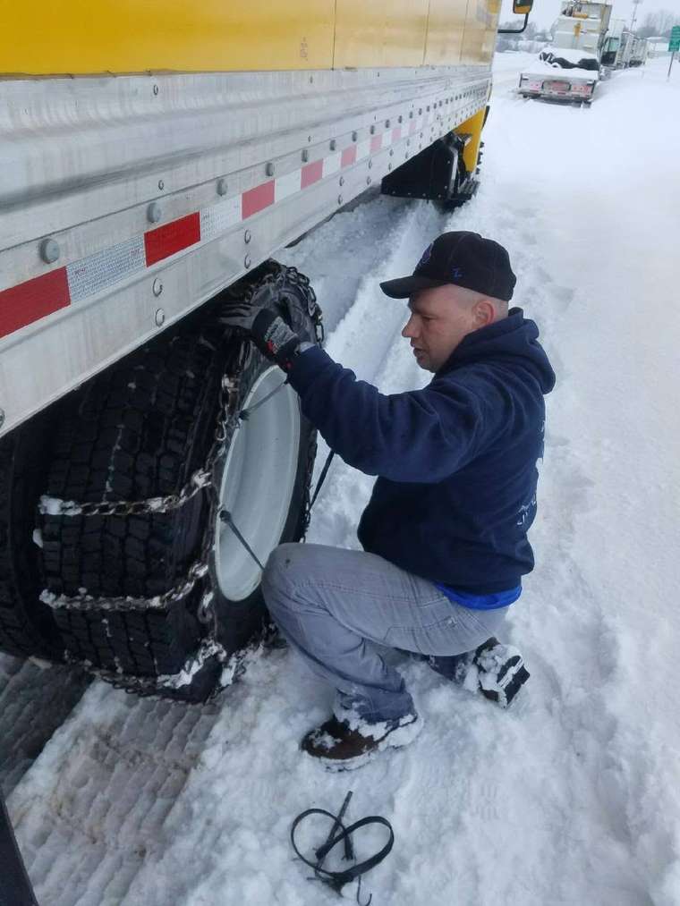 Delicate Touch crew fitting tire chains to a trailer on a winter interstate haul