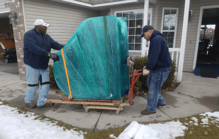 Delicate Touch crew moving a wrapped grand piano on a padded board