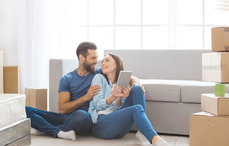 Stress-Free Moving in Idaho, ID – Delicate Touch Moving Happy couple sitting on the floor surrounded by moving boxes during their move in Idaho.