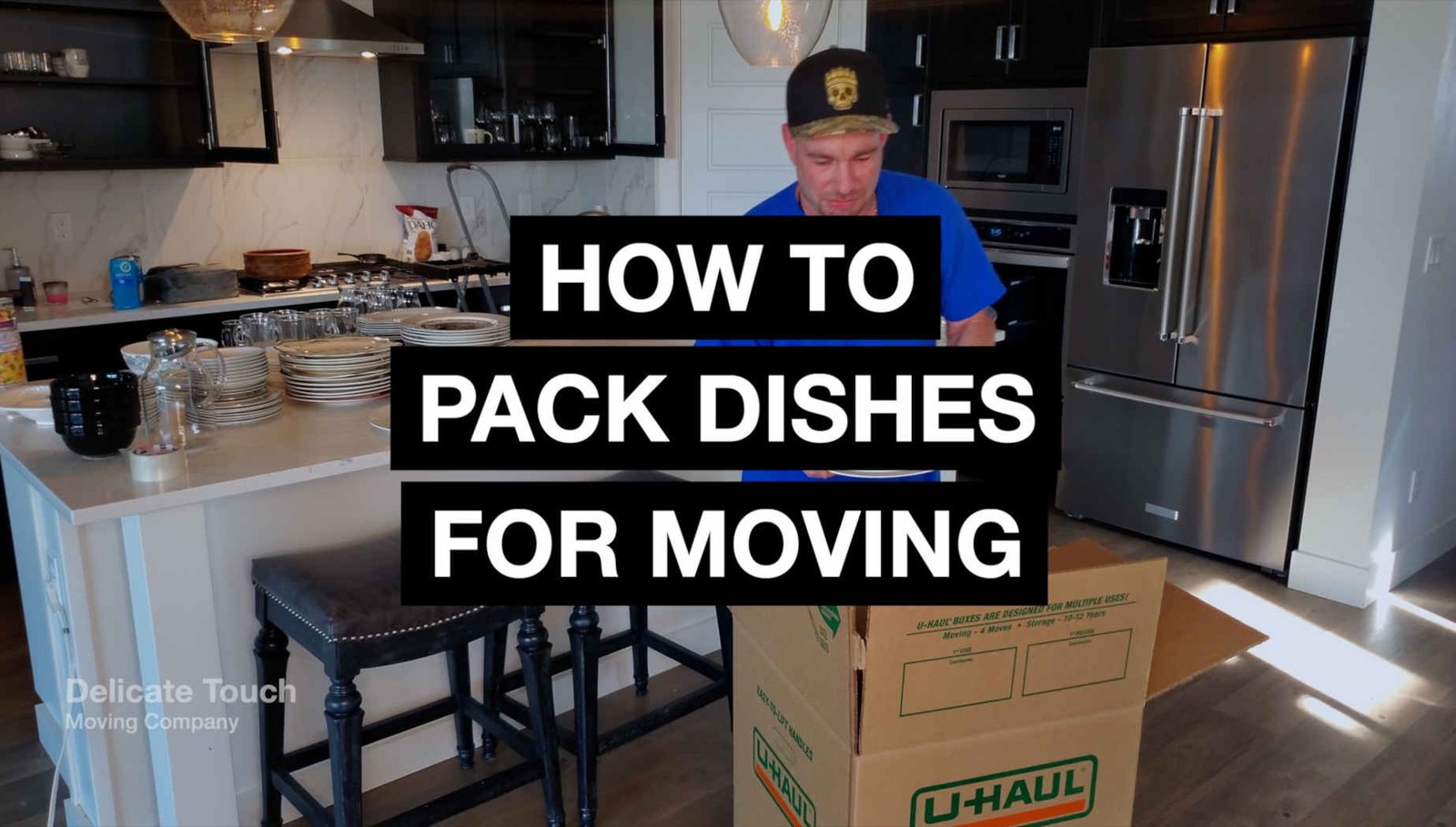 Person carefully packing dishes into a U-Haul moving box in a kitchen.